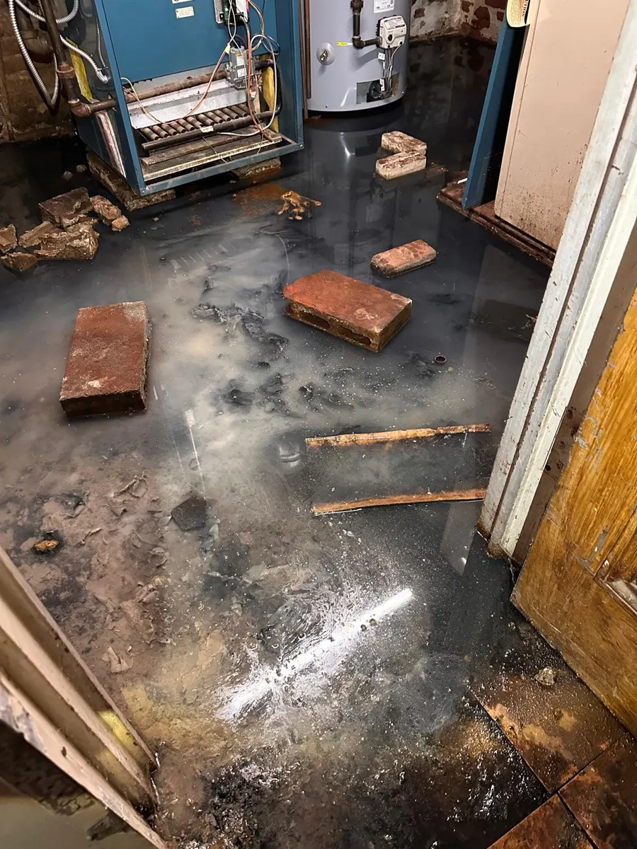 Sewage water and broken debris covering the floor of a basement boiler room after a cracked drain pipe in Cypress Hills, Brooklyn