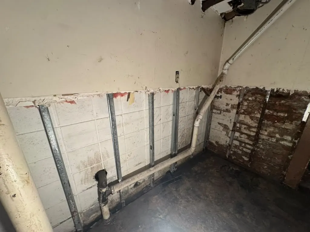 Basement walls opened to the steel studs, exposing the drain line after a sewage backup in Cypress Hills, Brooklyn