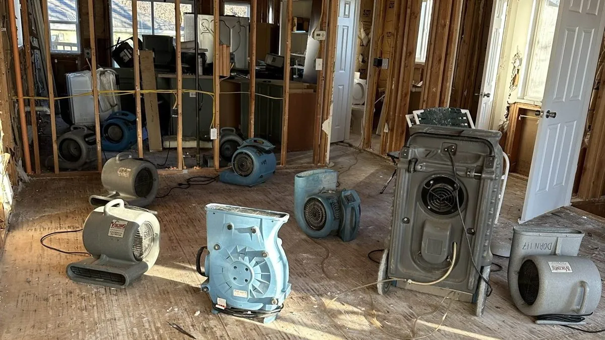 Air movers and a dehumidifier drying a room with the wet drywall cut out