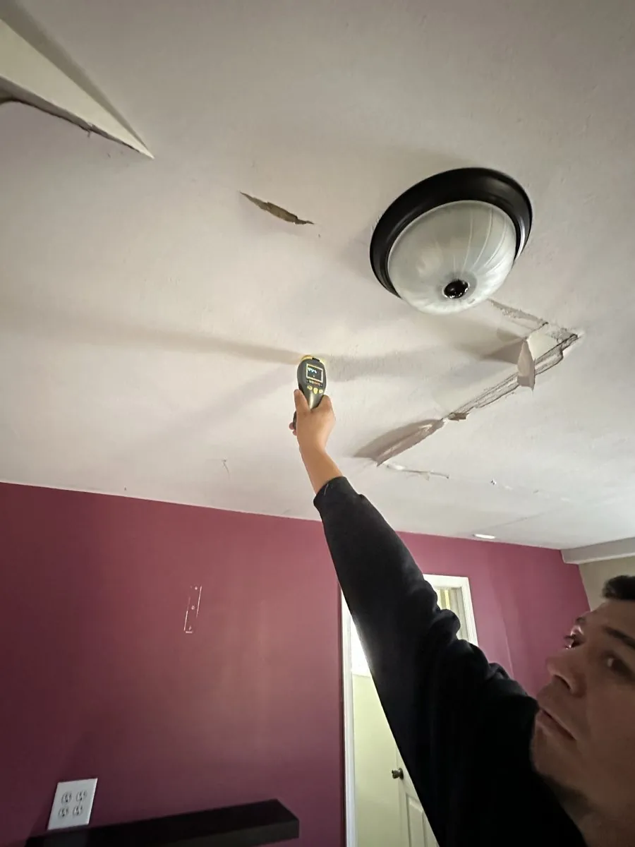 Moisture meter reading a water-stained ceiling below a leak