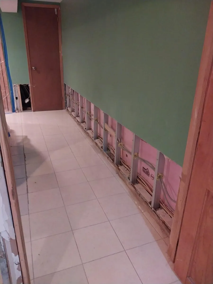 Basement hallway with wet drywall cut out at floor level, ready for drying after a water heater flood in Marine Park, Brooklyn