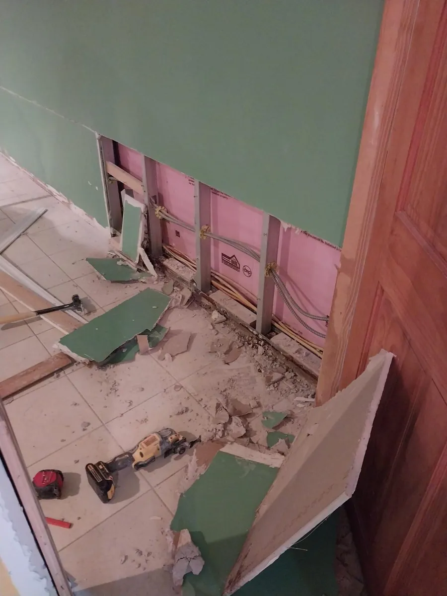 Flood cut on a finished basement wall exposing steel studs, wiring and pink foam insulation after a water heater leak in Marine Park