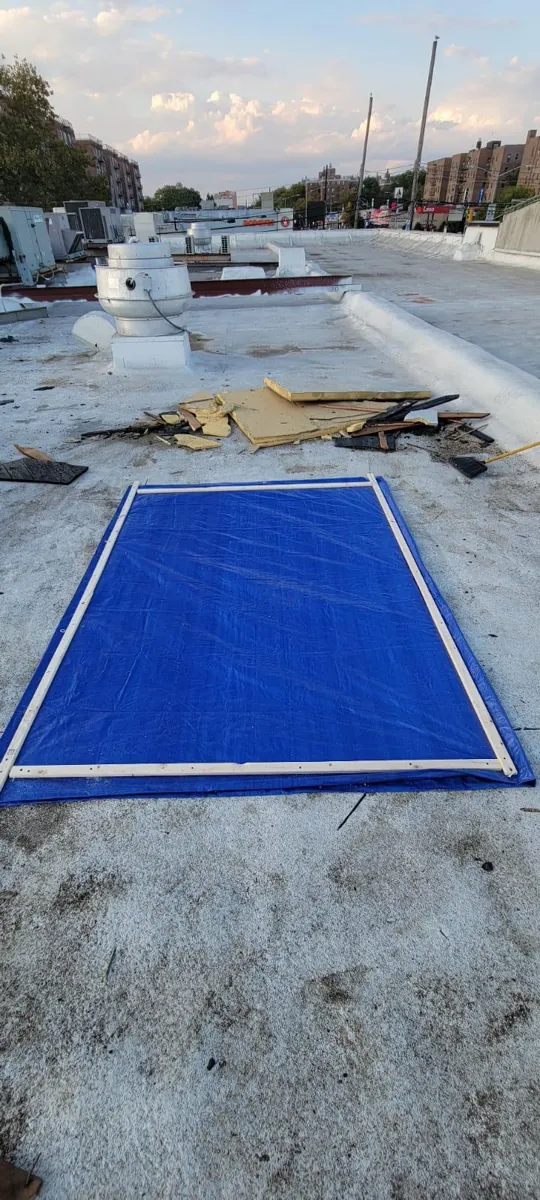 Blue tarp secured over a roof opening with a wood frame on a flat commercial roof