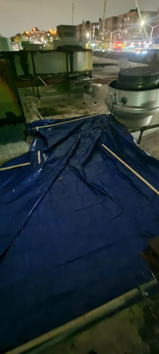 Blue tarp covering fire damage next to a rooftop exhaust fan