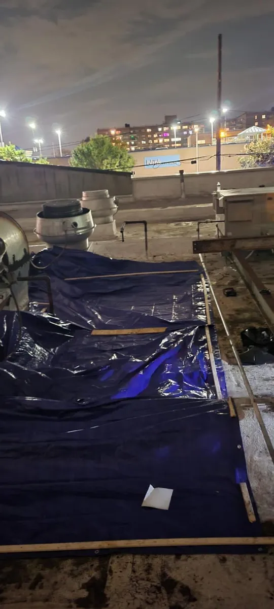 Several blue tarps held down with lumber across a section of flat roof